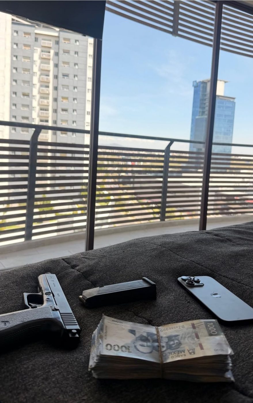 Arma, cargador, efectivo y teléfono sobre un sofá en un balcón con vista a torres